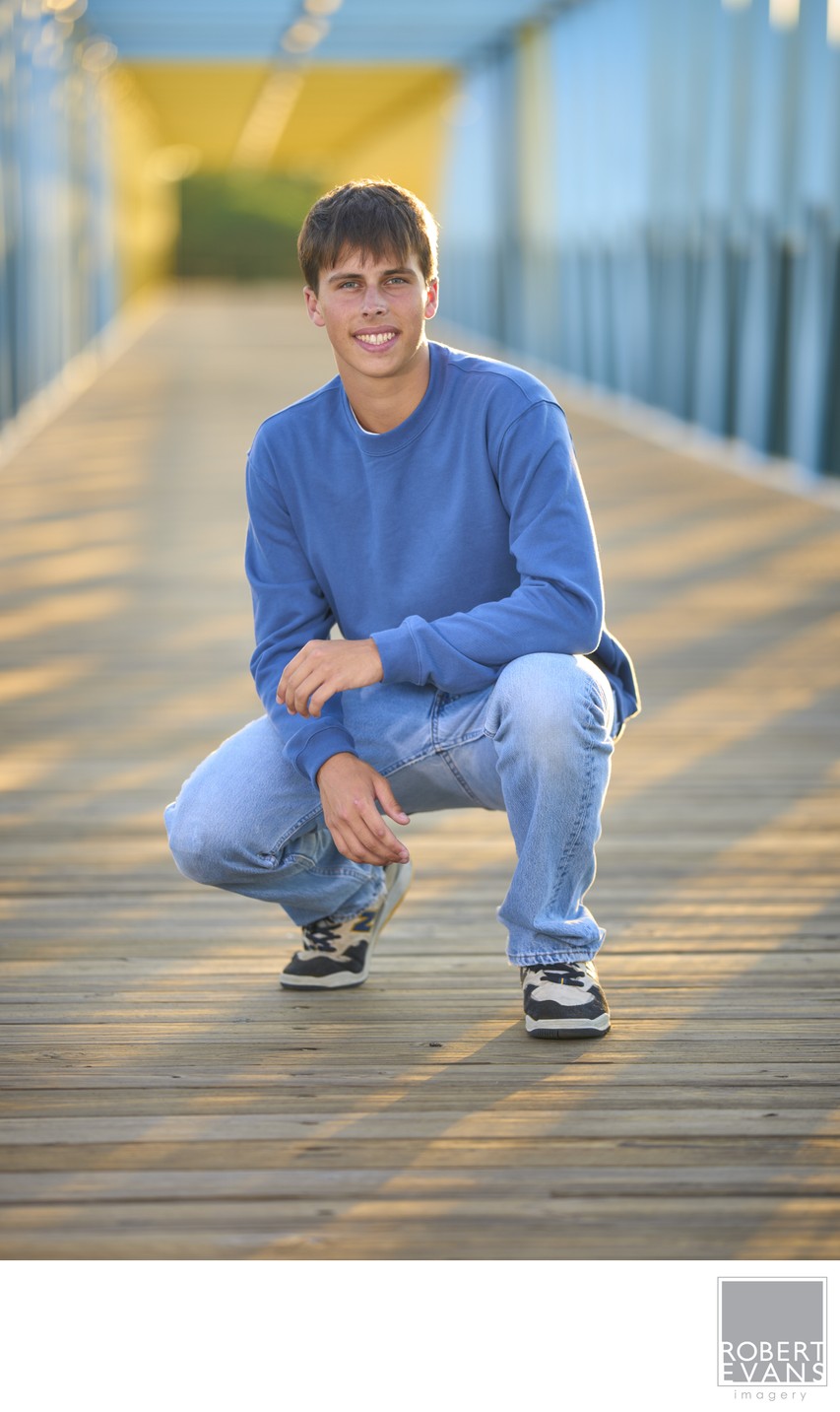 Senior portrait of a boy posing on a blue and yellow covered bridge