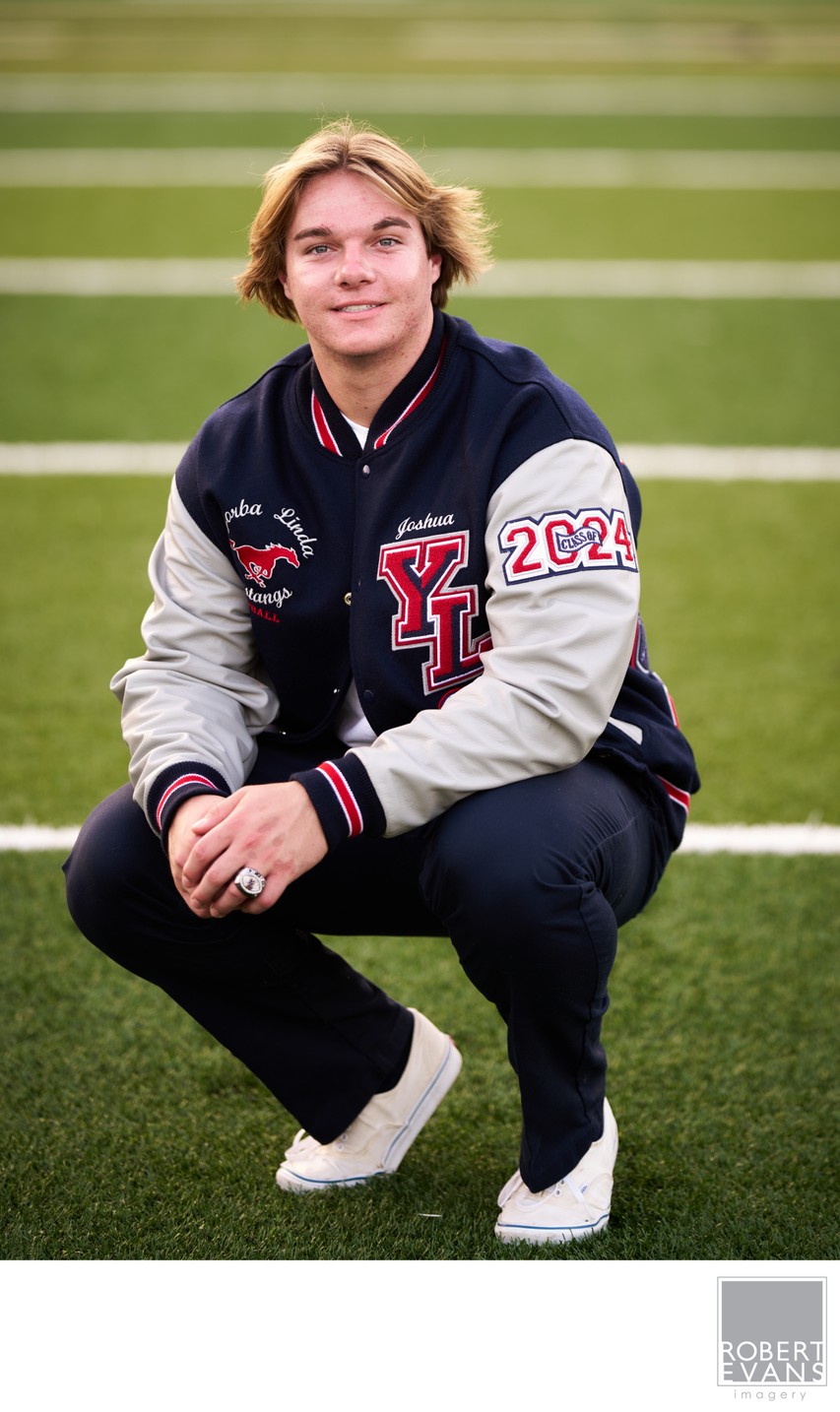 High School Senior Football Player  wearing his Letterman's jacket and class ring on the field.