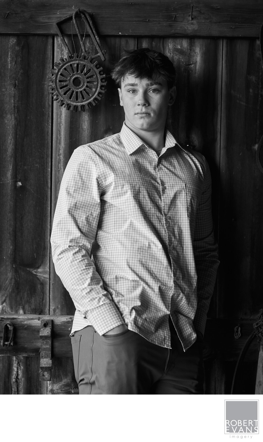 Dramatic black and white portrait of a high school senior boy in an old barn.