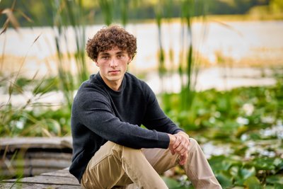 Portrait of a Senior boy sitting on an old dock at the edge of a lake. 