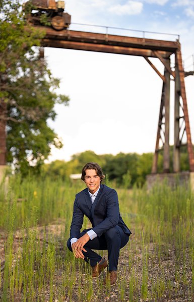Sharp dressed high school senior boy dressed in a blue suit near an old railroad bridge