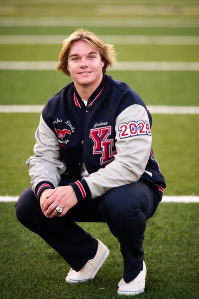 High School Senior Football Player  wearing his Letterman's jacket and class ring on the field.