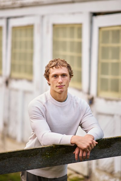  Delano senior portrait of a boy leaning on a fence post with weathered white wooden doors