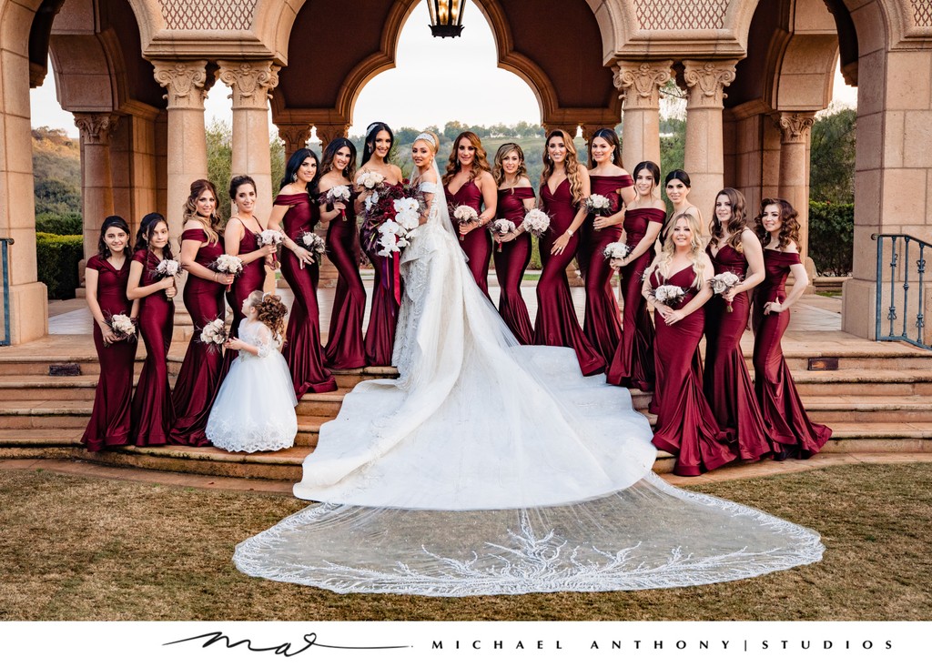 Bridal Party in Burgundy Gowns with Bride in Front of Elegant Archway