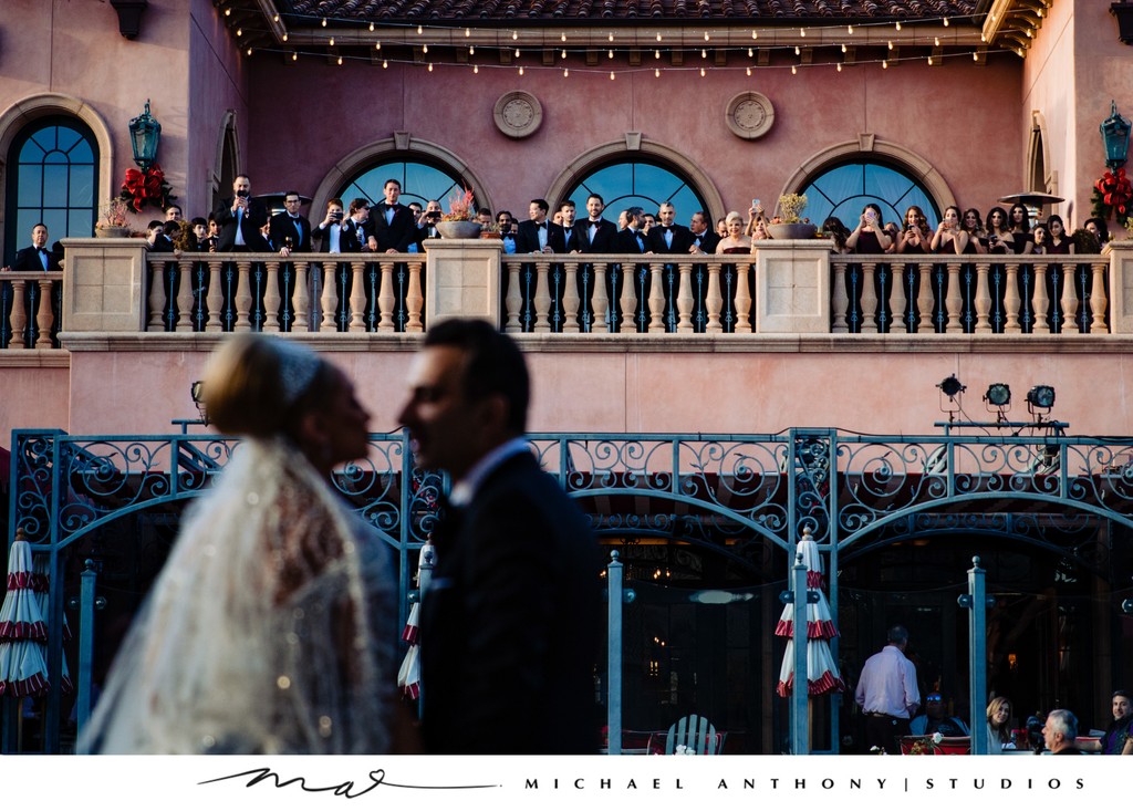 Bride and Groom Kissing with Guests Watching from Balcony