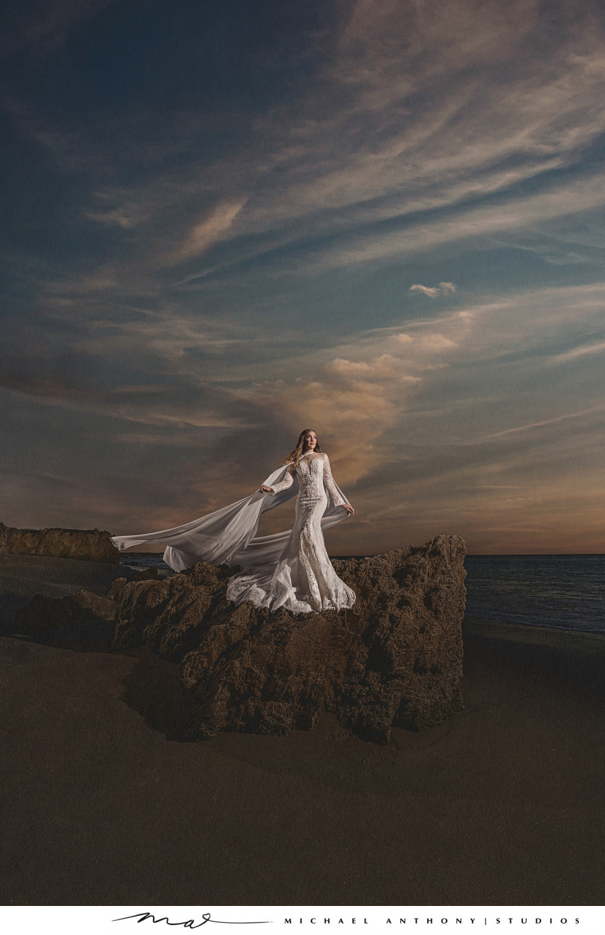 Bride stands on a rocky beach in dramatic wedding photo