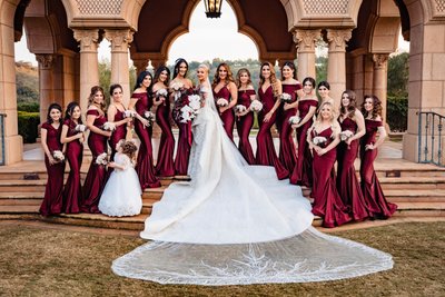 Bridal Party in Burgundy Gowns with Bride in Front of Elegant Archway