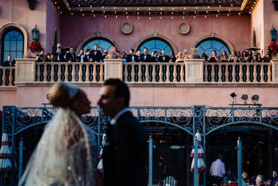 Bride and Groom Kissing with Guests Watching from Balcony