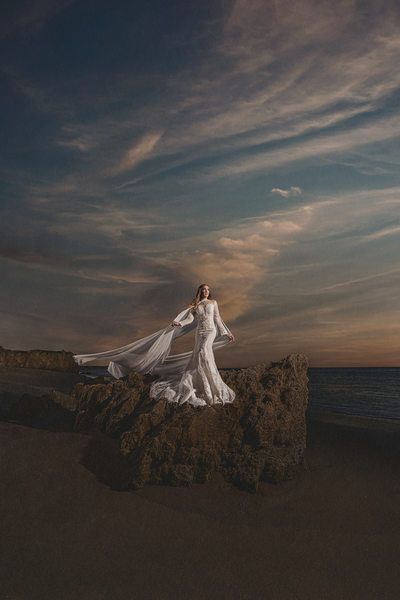 Bride stands on a rocky beach in dramatic wedding photo