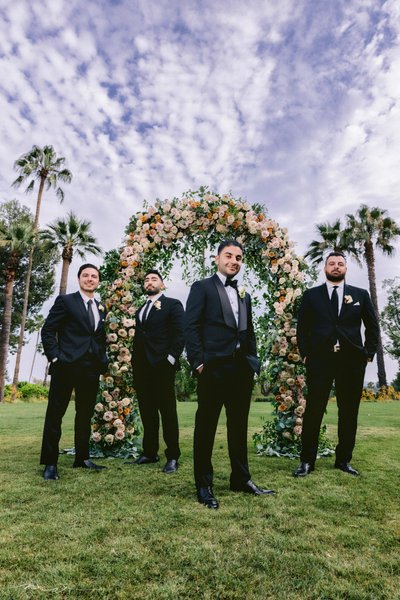 Stylish Groomsmen Under Floral Arch with Palm Trees