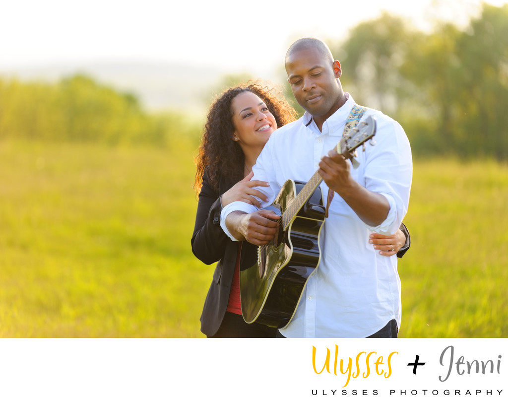 Engaged couple in field playing guitar