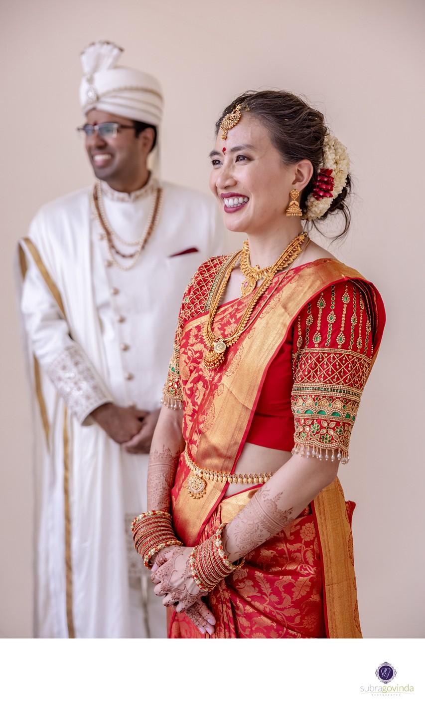 A candid portrait of Suzanne in a red and gold silk saree and Saravana in a white sherwani  at Sri Srinivasa Perumal Temple, Singapore