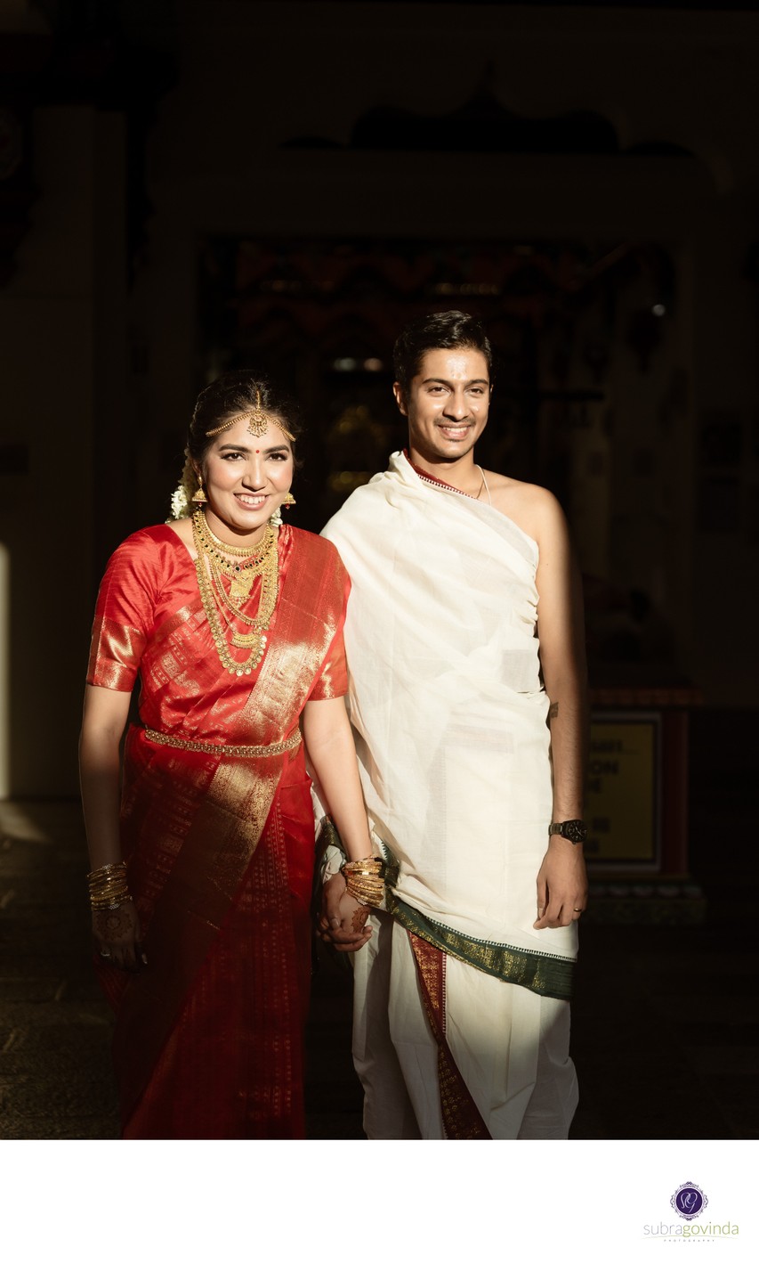 Vidya  in a red silk saree and Sidharth in a traditional veshti holding hands during a South Indian wedding ceremony at Sri Mariamman Temple, Singapore