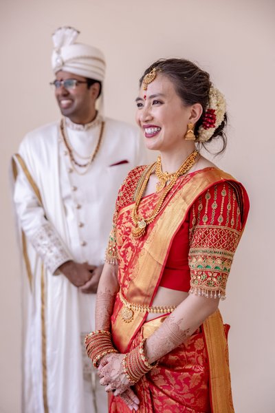 A candid portrait of Suzanne in a red and gold silk saree and Saravana in a white sherwani  at Sri Srinivasa Perumal Temple, Singapore