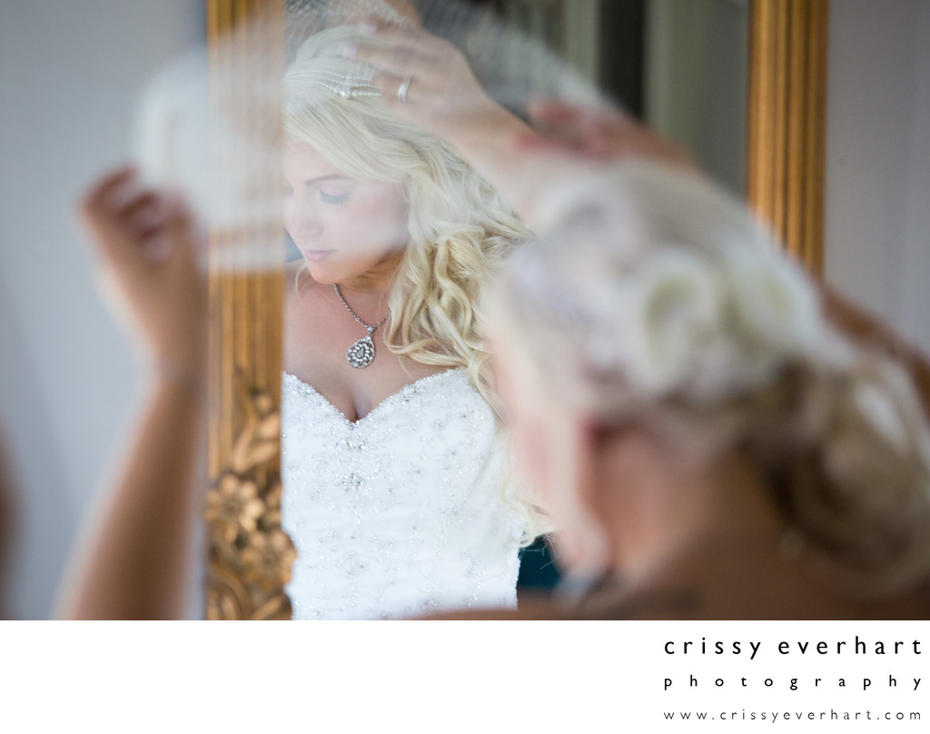 Bride putting on lace veil in gold mirror at Faunbrook