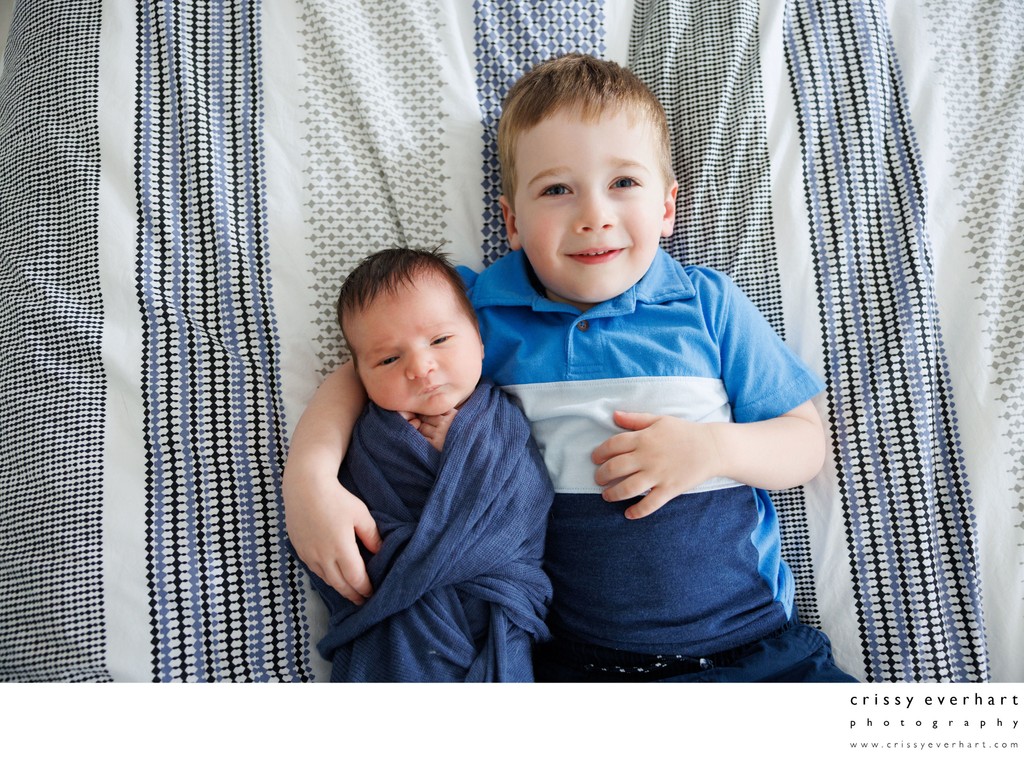Big Brother Holds Newborn on Bed