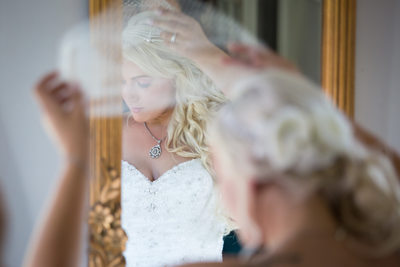 Bride putting on lace veil in gold mirror at Faunbrook