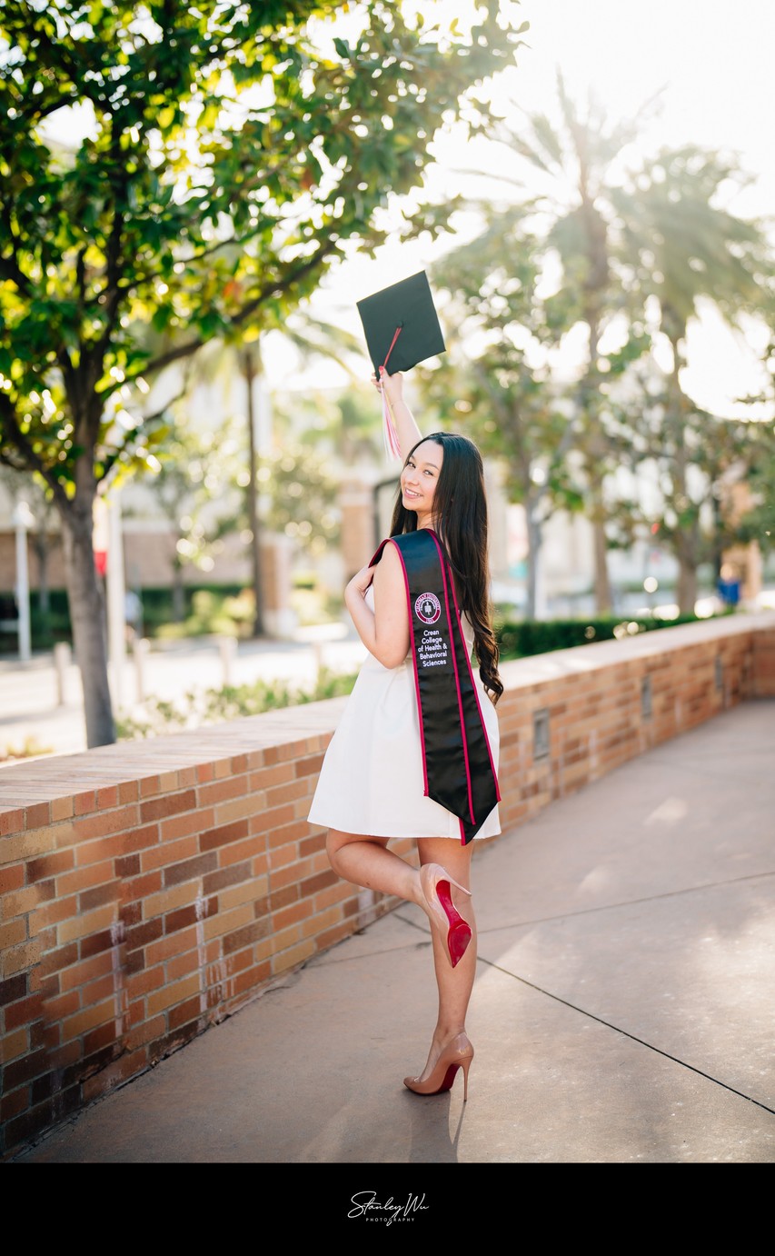 Chapman University grad photo, cap raised, brick path