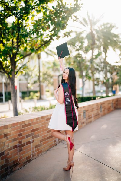 Chapman University grad photo, cap raised, brick path