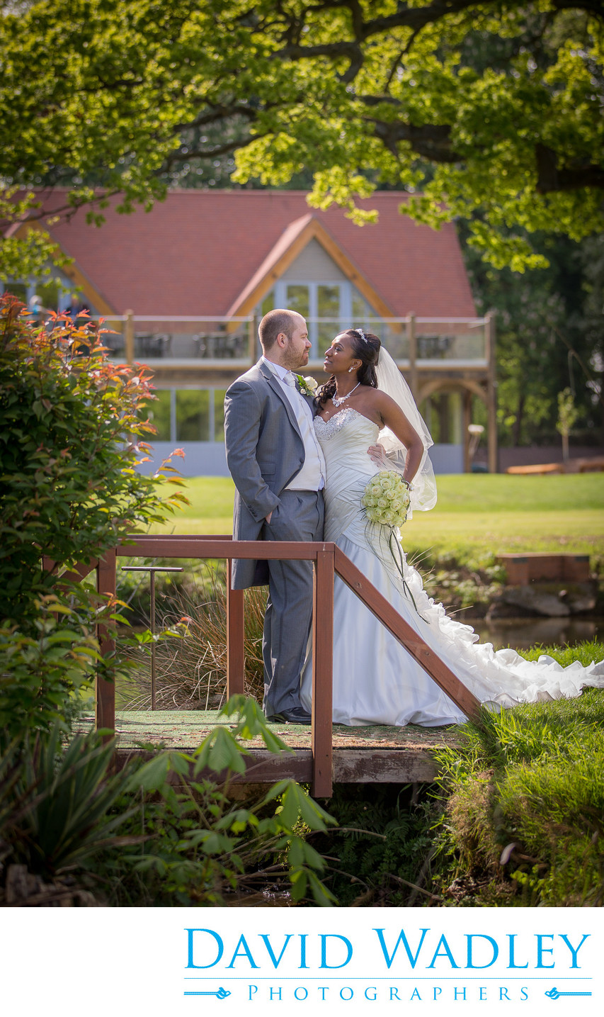 Bride & Groom on bridge with clubhouse at Nailcote Hall.