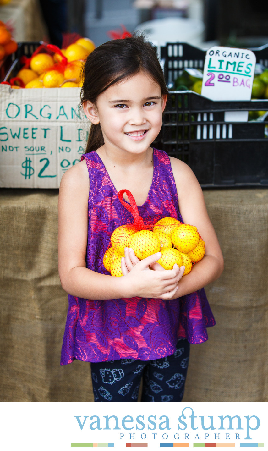 Smiling portrait of young girl at a farmers market holding lemons