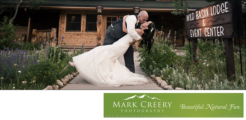 Groom dipping & kissing bride in front of Wild Basin Lodge