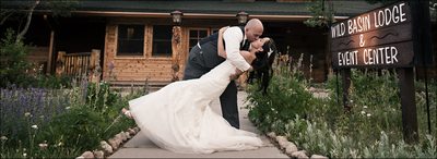Groom dipping & kissing bride in front of Wild Basin Lodge