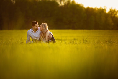 Engaged couple sitting in field at sunset