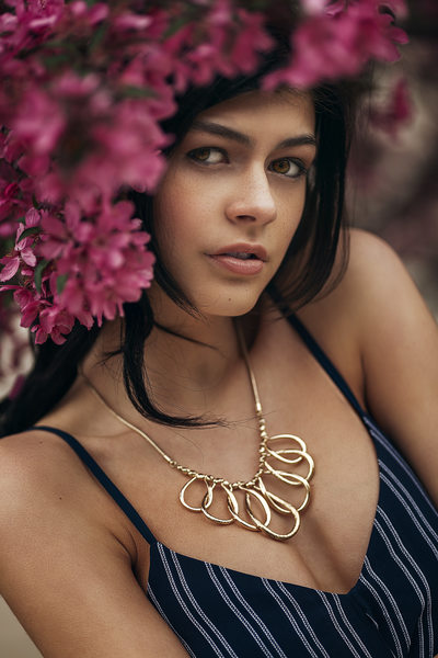 Brunette posing with pink flowers and gold necklace