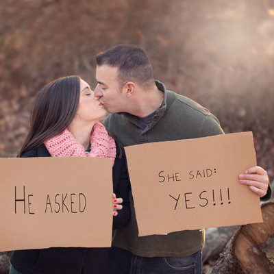 engaged couple kissing and holding cardboard signs
