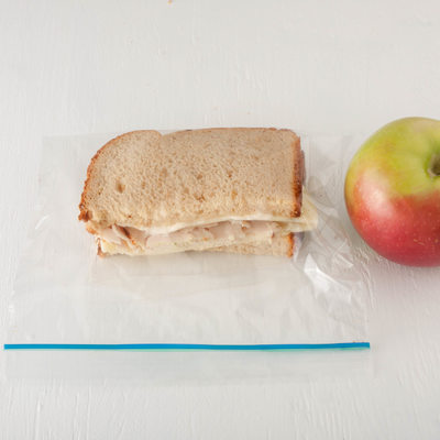 turkey sandwich in a plastic bag with apple isolated on white background