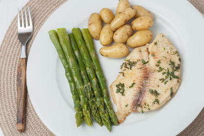 cooked fish with parsley servied with asparagus and baby potatoes on white plate