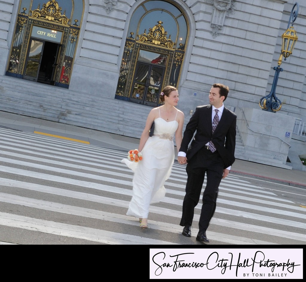 Happy newly married couple walk across the street in front of SF City Hall