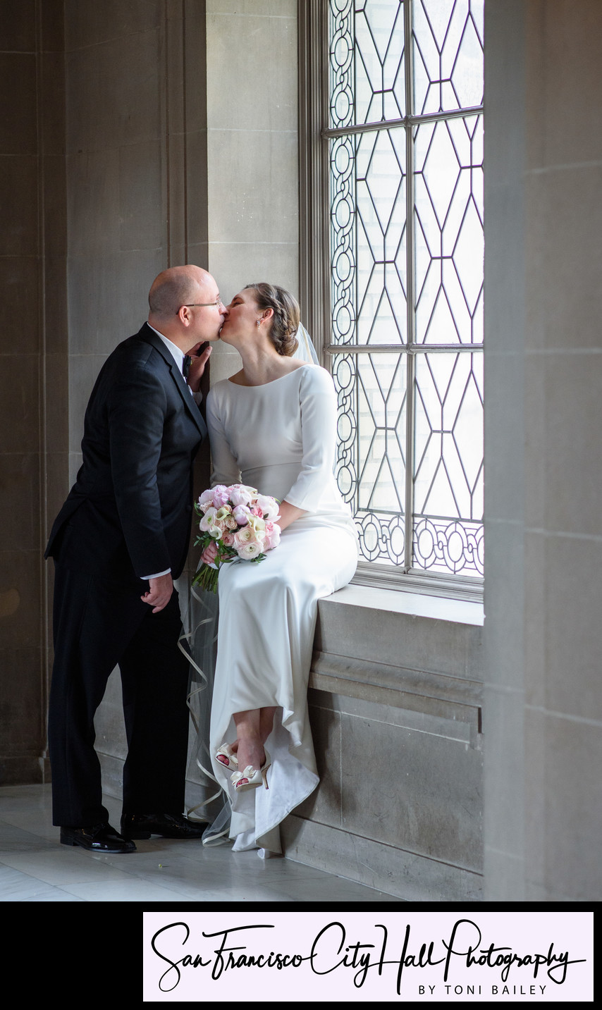 bride and groom kissing in window light at third floor window
