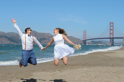 A LGBTQ  Couple jumping at Baker Beach with the Golden Gate Bridge