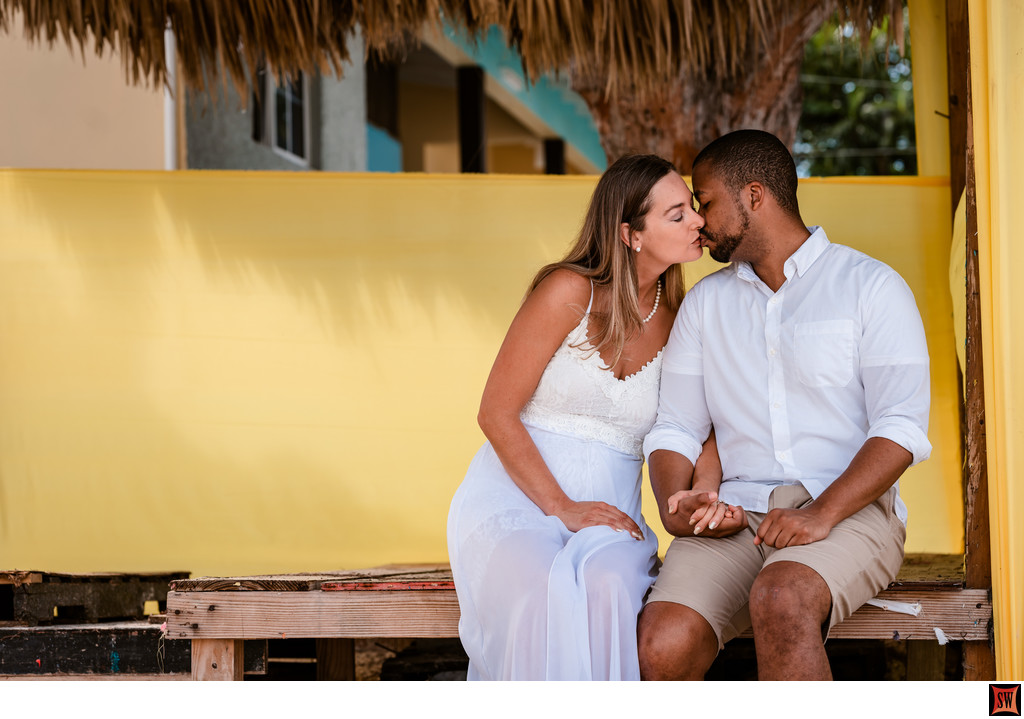 engaged couple kisses against colorful background