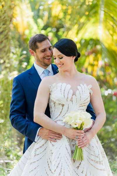 bride and groom hold each other close in lush tropical