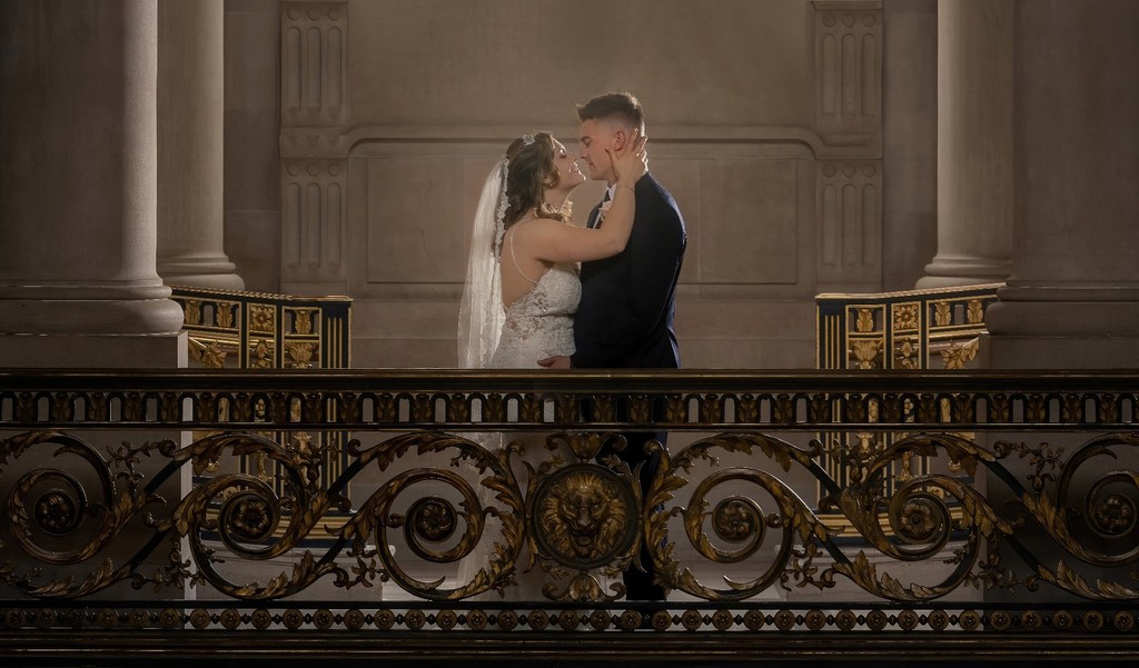 Newlyweds share an intimate moment on a balcony with ornate railing.