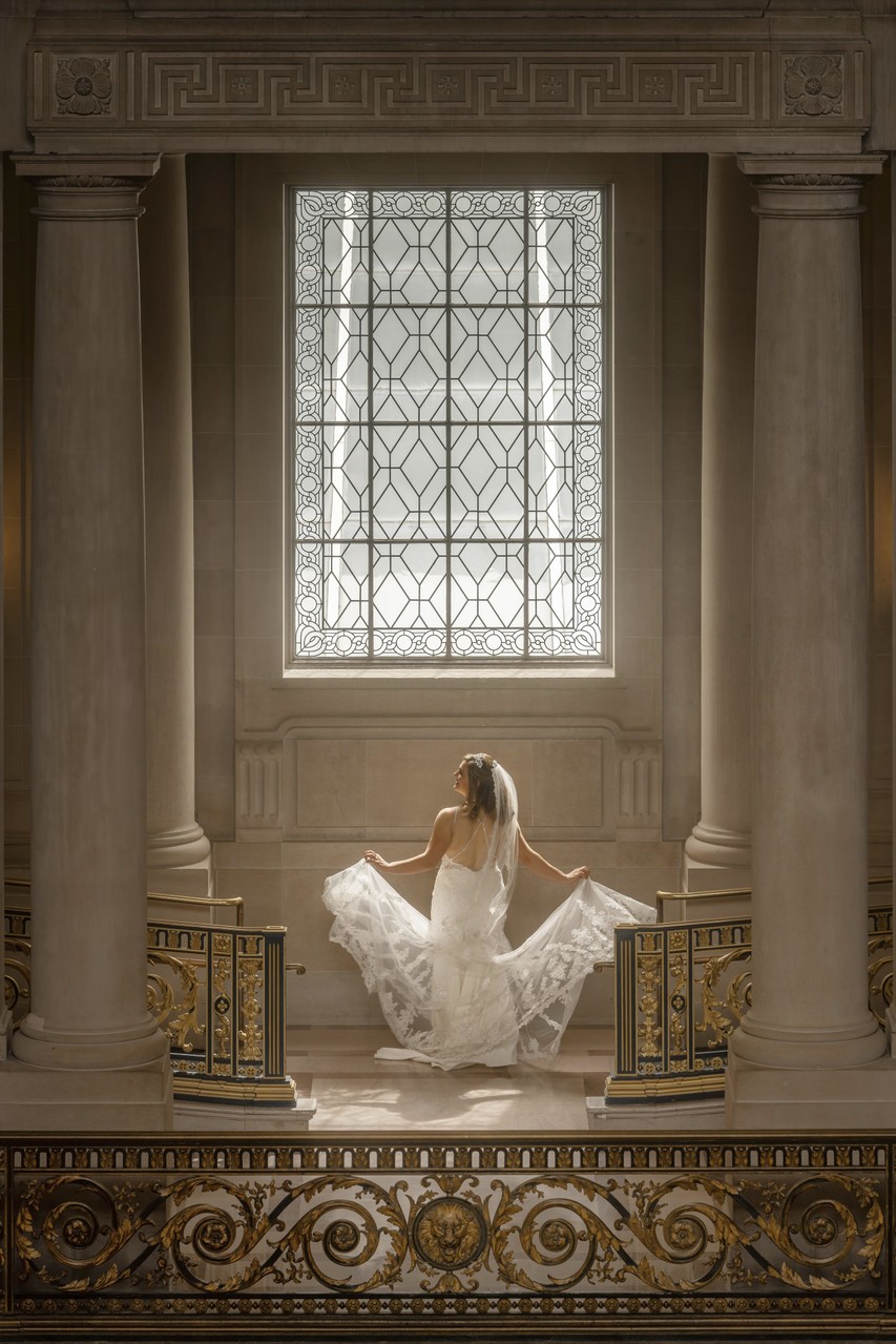 Bride in White Dress Before Ornate Window in Grand Hall