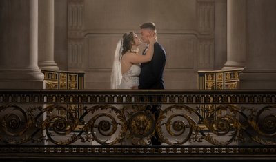 Newlyweds share an intimate moment on a balcony with ornate railing.