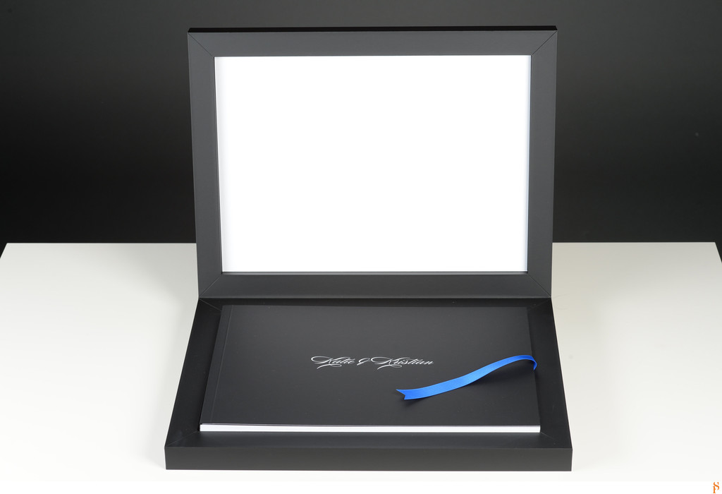 BLACK WEDDING ALBUM WITH WHITE WRITING ON TOP AND BLUE RIBBON