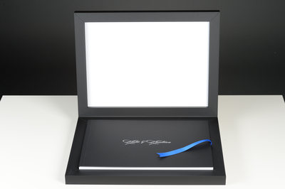 BLACK WEDDING ALBUM WITH WHITE WRITING ON TOP AND BLUE RIBBON