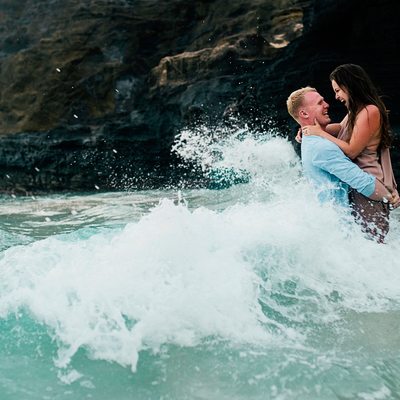 Ocean waves washing over happy embraced couple
