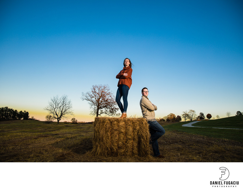 Engaged couple posing on a bale of hay