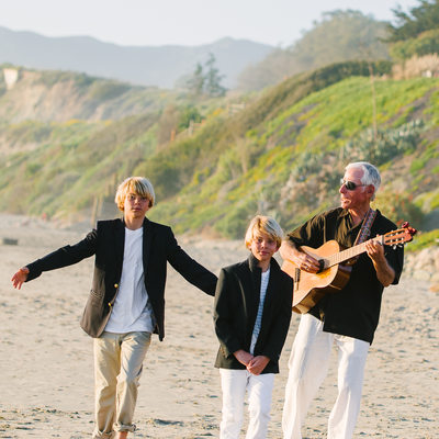 grandfather on beach playing guitar to his grand kids 
