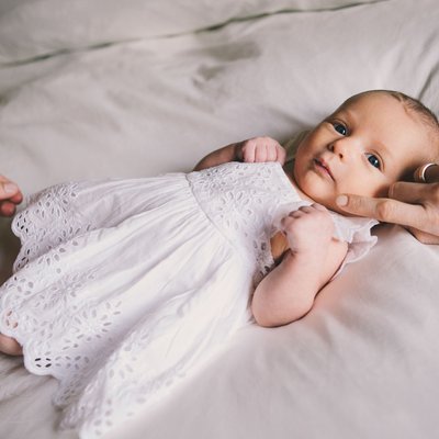 Baby girl on bed with white dress with parents hands