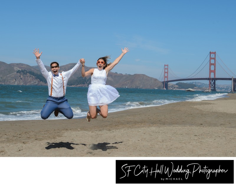 Lesbian newlyweds jumping together at Baker Beach in San Francisco