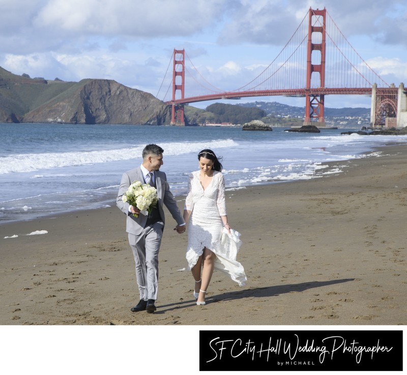 Newlyweds walking on Baker Beach with Golden Gate bridge in the background