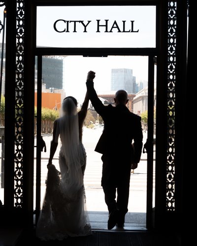 Excited San Francisco city hall newlyweds exit the building with arms raised