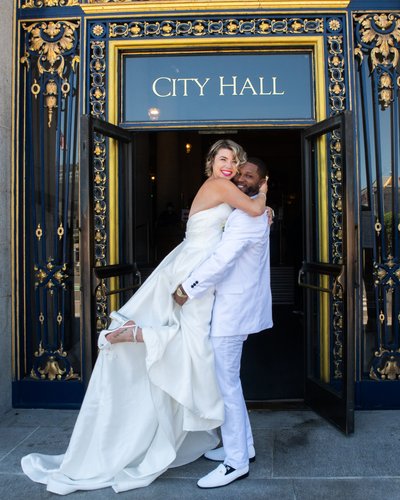 Groom lifting bride at San Francisco city hall sign